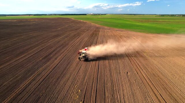 Agricultural Tractor on Plowing field, aerial view. Plowing field. Red Tractor with Plough on Plowed. Ploughing, Soil Tillage. Soil tillage, Cultivated land. Tractor soil cultivator
