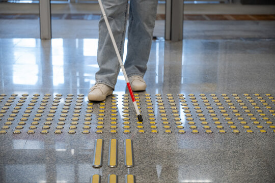 A blind woman walks on tactile paving. Close-up of her feet and a walking stick.