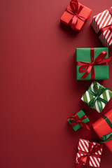 Naklejka premium Stack of red and green Christmas presents with ribbons and striped wrapping on vertical maroon red background