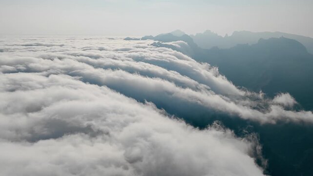 Aerial view above moving cloud layer in mountains. Clouds partially cover ridges and valleys