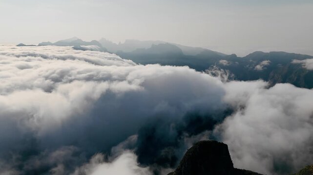 Dense clouds moving among mountain peaks and partially covering valleys. Aerial view above cloud layer