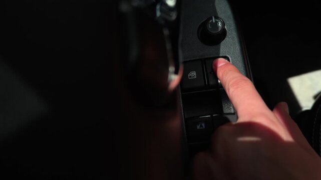 Overhead close-up of a driver pressing the door lock button on the vehicle door control panel. The finger activates the locking control beside the window switches and side mirror adjustment