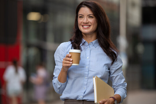 Confident businesswoman walking with coffee and folder in city