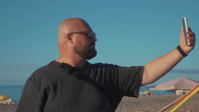 Man recording selfie video on beach with smartphone for social media during summer vacation. Travel vlogger filming selfie clip.