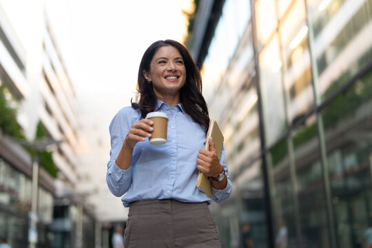 Professional woman walking downtown with coffee and notebook