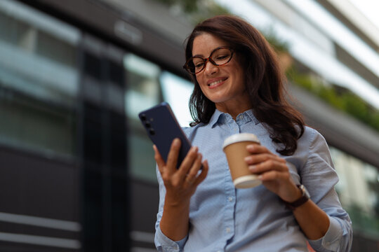 Businesswoman using smartphone and drinking coffee to go