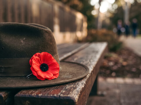 A somber hat adorned with a single red poppy rests on a weathered wooden bench, evoking a sense of remembrance and sacrifice