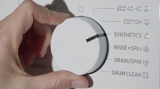 Hand turning washing machine program selector knob. Woman's hand turning the selector knob on a modern washing machine control panel, choosing a washing cycle such as eco, cotton, or synthetics