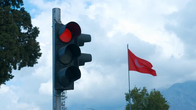 Turkish flag waving near a red traffic light. Crimson traffic signal standing near waving national flag of turkey, highlighting urban street scenery under cloudy atmospheric conditions
