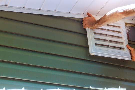 Person installs vent cover on side of house in construction