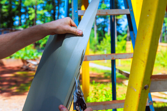 Cutting piece of PVC siding sheet on ladder in backyard