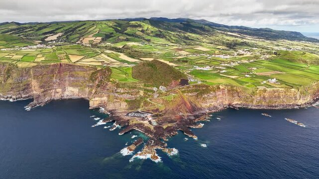 Ponta da Ferraria from above on Sao Miguel, Azores, Portugal. Ferraria thermal spa beside Atlantic Ocean beneath volcanic cliffs and patchwork farmland in green island hills
