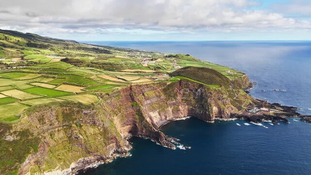 Patchwork fields cover coastal hills of Sao Miguel, Azores, Portugal, above Atlantic Ocean. Aerial view of rural island landscape and farmland along steep volcanic cliffs