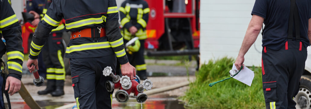 Firefighters Working Together Carrying Hoses And Hydrant Manifold Near Fire Truck During Emergency Response