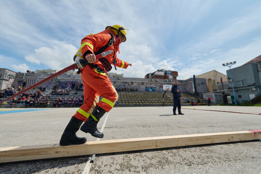 Firefighter Training Drill Balancing On Beam While Carrying Hose During Outdoor Emergency Exercise