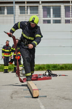 Firefighter Training Drill With Helmeted Firefighter Running With Hose Over Balance Beam During Exercise