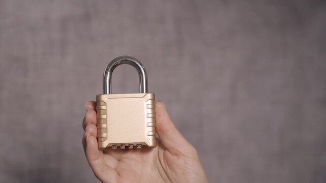 Woman's hand holding golden combination padlock for security