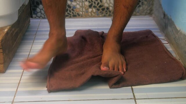 a person's feet standing on a brown towel on a tiled bathroom floor