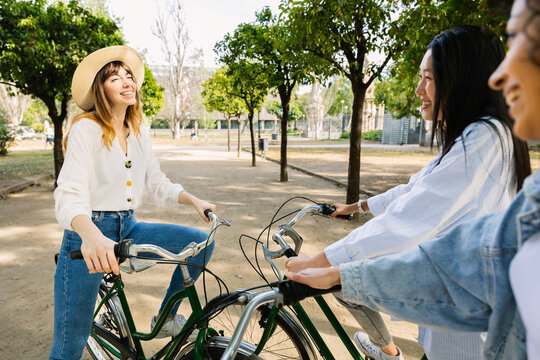 Young group of multiracial women friends chatting closely by a bicycle together outdoors in the city. Friendship and travel concept.