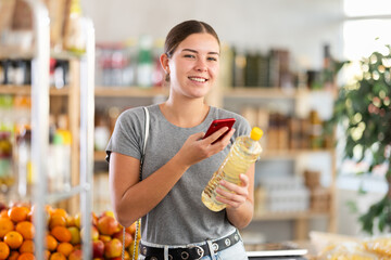 Girl in store scan QR code and study oil assortment. With help of mobile app, buyer receive...