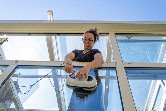 Focused woman operating a robotic window cleaner from a glass balcony