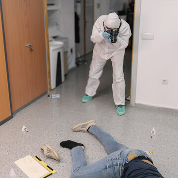 Forensic photographer documenting a body at an indoor crime scene