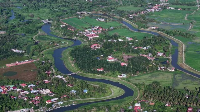 Aerial river winds through green fields. Red roofed homes dot the landscape at Kubang Semang