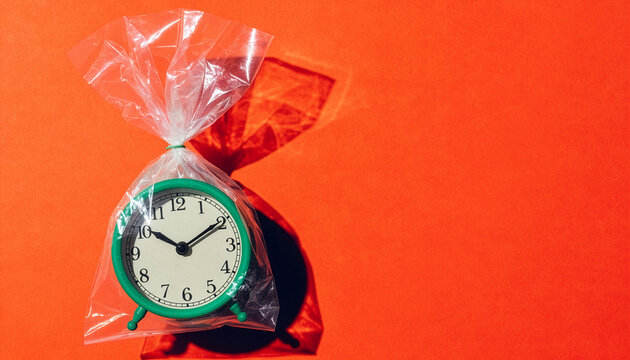 Green alarm clock sealed in clear plastic bag on orange background