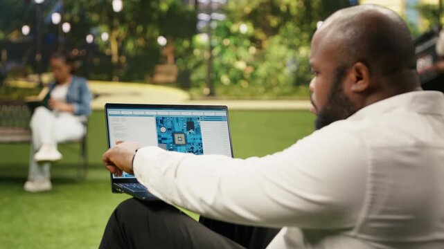 Businessman uses laptop software with a microchip and circuit board interface in a city park, illustrating semiconductor engineering, hardware monitoring and remote technology work.