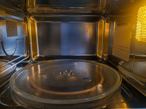 A pristine, empty microwave oven interior glows with warm golden light over its glass turntable and sleek stainless steel walls, evoking a quiet kitchen atmosphere. Nobody is present.