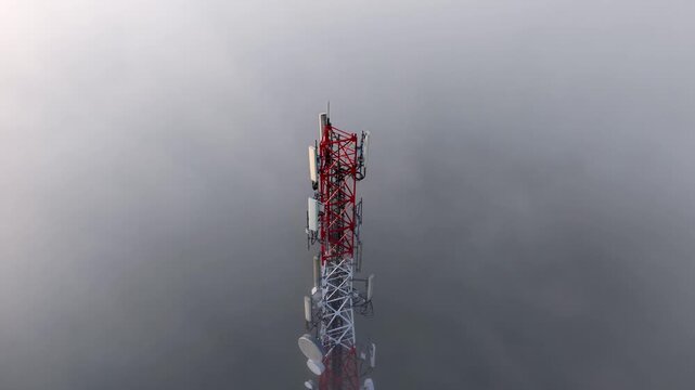 Aerial view of a red telecom tower piercing through dense fog