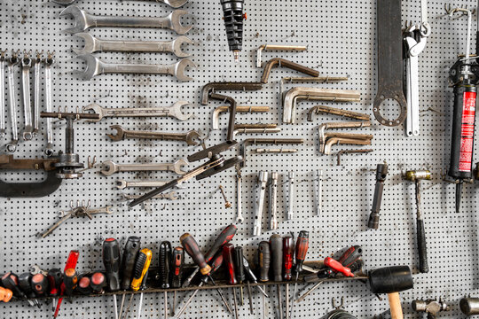Organized collection of hand tools including wrenches, screwdrivers, hex keys and hammers hanging on a pegboard inside a workshop.