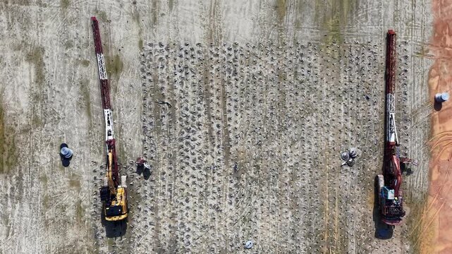 Aerial showing two drilling machines operating on a barren field with visible patterns of holes in the soil