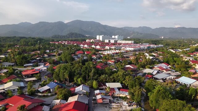 Aerial shot of a peaceful residential area with vibrant red roofs surrounded by lush green trees and hills at Balik Pulau