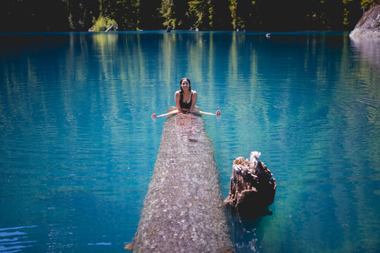 Woman sitting on a fallen log in a turquoise glacial lake, British Columbia