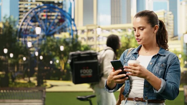 Worried woman stands in a city park waiting impatiently and checking time on a mobile phone, appearing concerned and agitated while running late and illustrating time pressure and anxiety outdoors.
