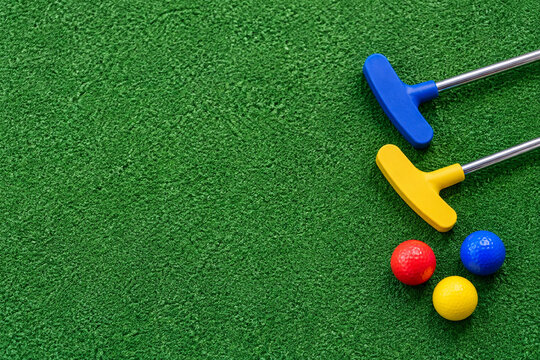 Colorful mini golf putters and balls on green turf viewed from above