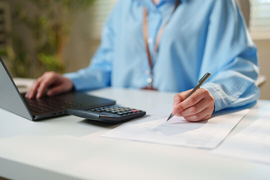 Accountant cross-referencing financial spreadsheets on a laptop while verifying printed ledger numbers with a calculator, automated cloud bookkeeping, invoice management, digital payroll solutions