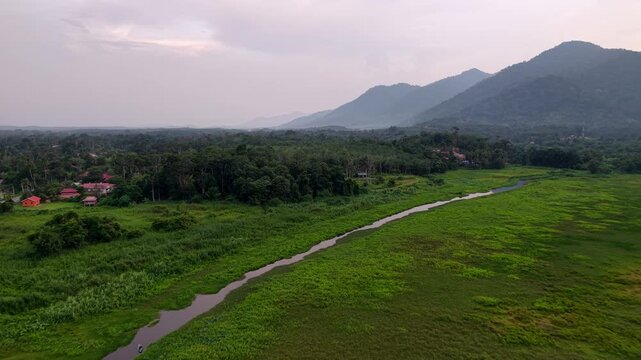 Aerial view captures lush green fields and mountains. River meanders through the countryside at Tasik Raban
