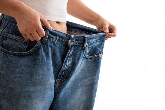 Woman holding oversized blue jeans showcasing significant weight loss results