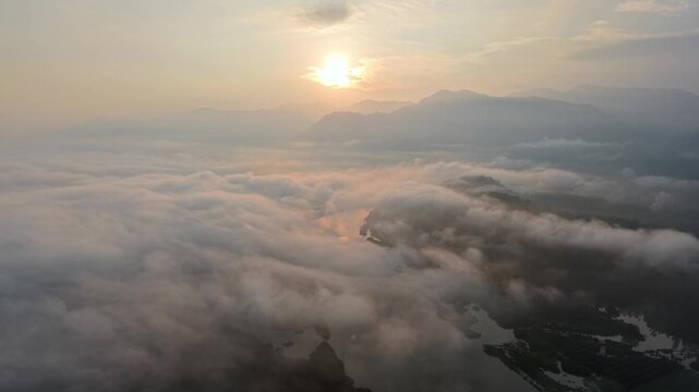 Aerial view of sun rising over mountain peaks. Soft morning light illuminates billowing clouds at Tasik Raban