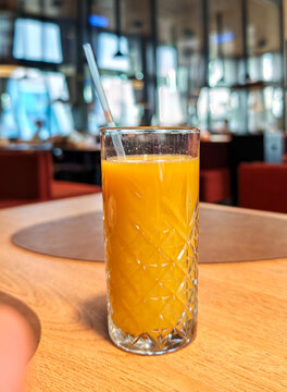 Tall glass of freshly squeezed orange juice with a straw on a wooden table.