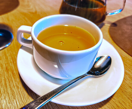 A white cup of hot yellow tea on a saucer.