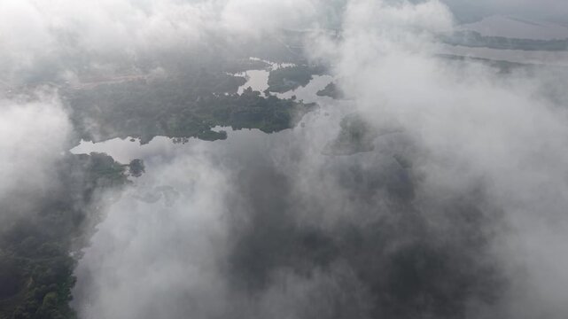 Aerial dense white clouds drifting over a lush green forest area and waterbody under natural daylight at Tasik Raban