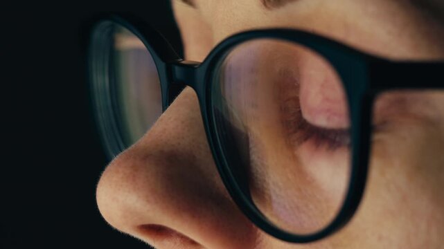 Close up of tired woman working at night on laptop, girl in eye glasses with reflections overworking busy, using computer in dark office