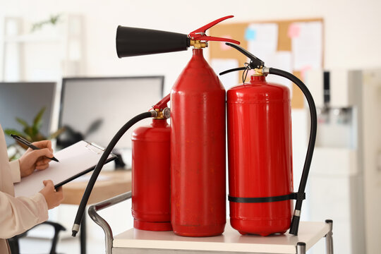 Fire safety inspection and workplace compliance, inspector checking fire extinguishers with a clipboard in an office environment for hazard prevention