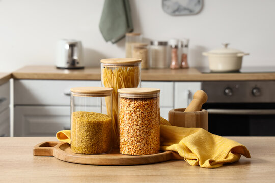 Sustainable kitchen organization and zero waste lifestyle, glass jars with dry food staples and wooden lids on a wooden cutting board in a home kitchen