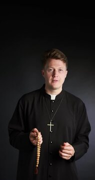 Priest in cassock with rosary on black background
