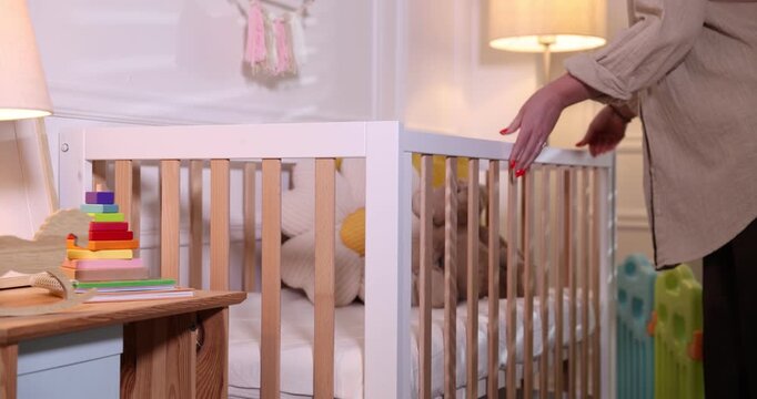Woman taking toy bear out of crib in baby's room, closeup