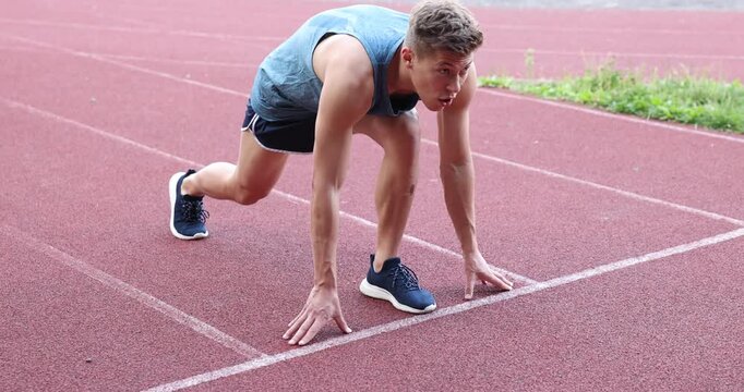 Athlete man getting into start position and running at stadium. Camera tracking